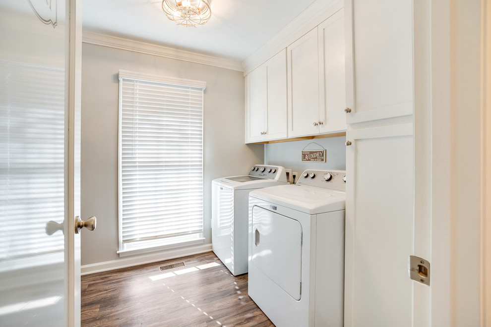 Photo of a small transitional galley utility room in Birmingham with shaker cabinets, white cabinets, grey walls, vinyl floors, a side-by-side washer and dryer and brown floor.