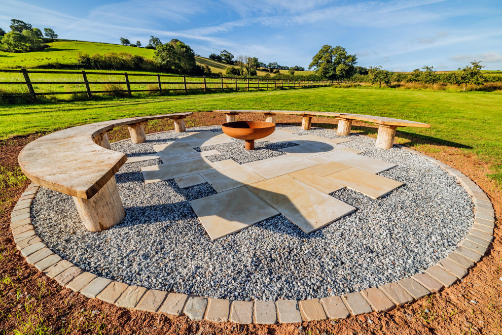 This is an example of a large country backyard patio in Devon with a fire feature and natural stone pavers.