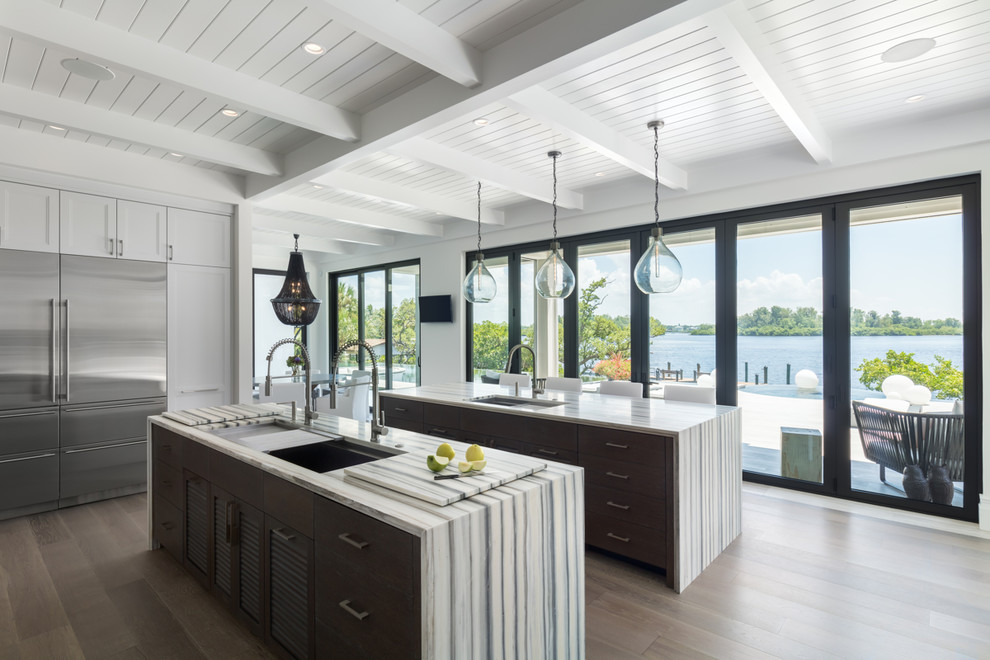This is an example of a beach style kitchen in Tampa with an undermount sink, shaker cabinets, white cabinets, stainless steel appliances, light hardwood floors, multiple islands and multi-coloured benchtop.
