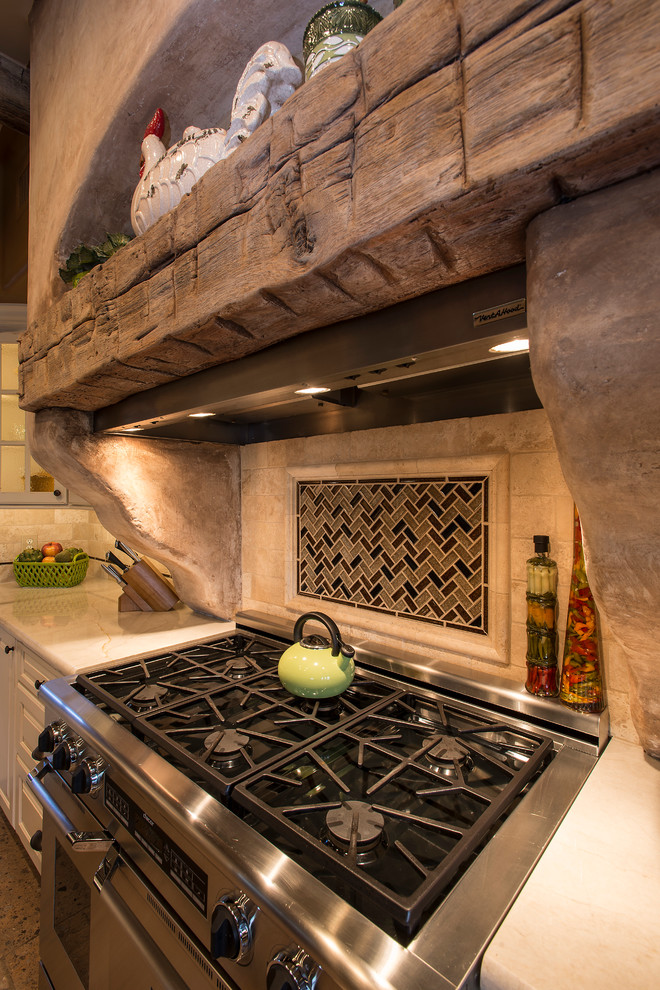 Large mountain style l-shaped travertine floor open concept kitchen photo in Phoenix with a farmhouse sink, raised-panel cabinets, white cabinets, granite countertops, beige backsplash, stone tile backsplash, stainless steel appliances and an island
