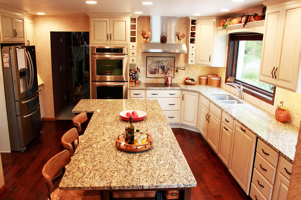 Kitchen - mid-sized traditional medium tone wood floor kitchen idea with an undermount sink, raised-panel cabinets, white cabinets, granite countertops, beige backsplash, cement tile backsplash, stainless steel appliances and an island