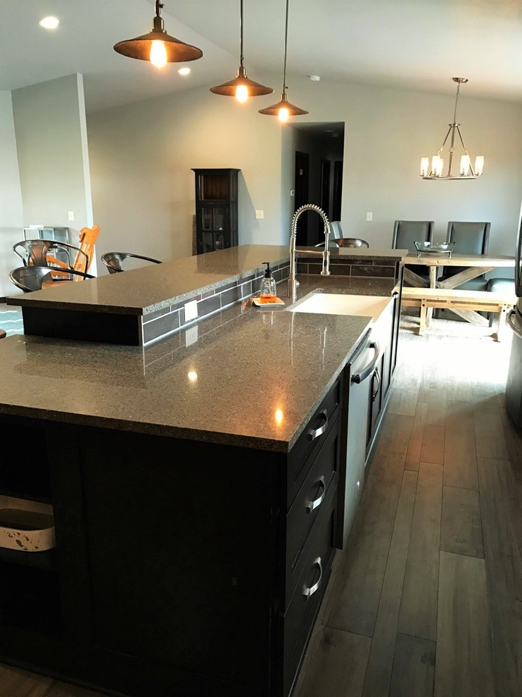 Example of a mid-sized transitional single-wall light wood floor open concept kitchen design with shaker cabinets, dark wood cabinets, multicolored backsplash, glass tile backsplash, stainless steel appliances, an island, a farmhouse sink and granite countertops