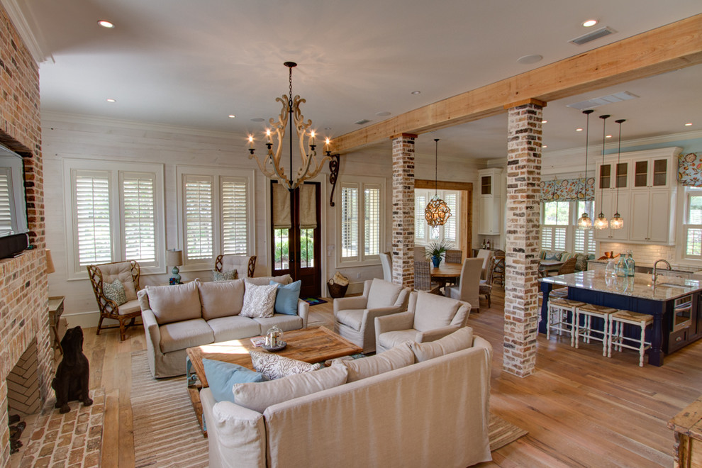 Inspiration for an expansive beach style open concept family room in Miami with white walls, light hardwood floors, a brick fireplace surround and a wall-mounted tv.