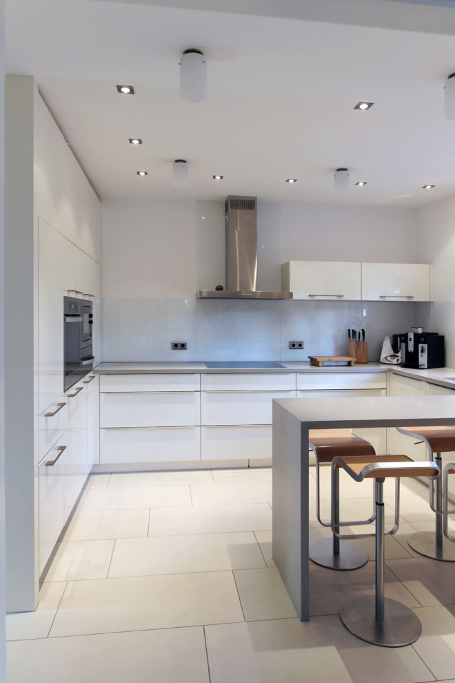 Photo of a mid-sized contemporary u-shaped kitchen in Dortmund with an undermount sink, flat-panel cabinets, white cabinets, white splashback, glass sheet splashback, panelled appliances, porcelain floors, a peninsula, beige floor and grey benchtop.