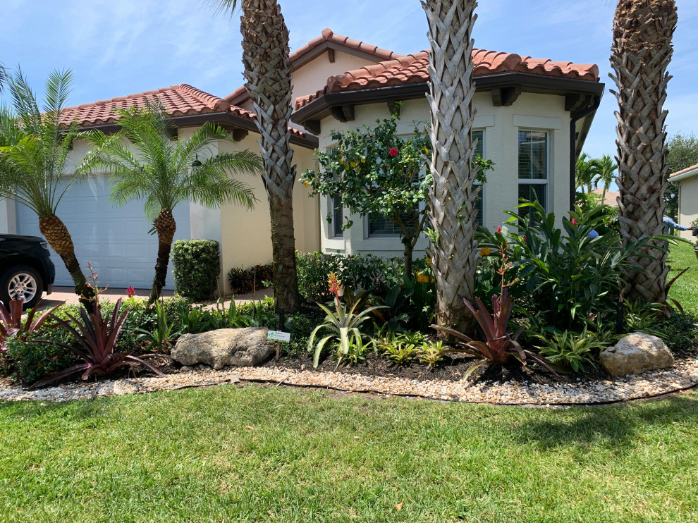 This is an example of a small tropical front yard partial sun xeriscape in Miami with with flowerbed and river rock.