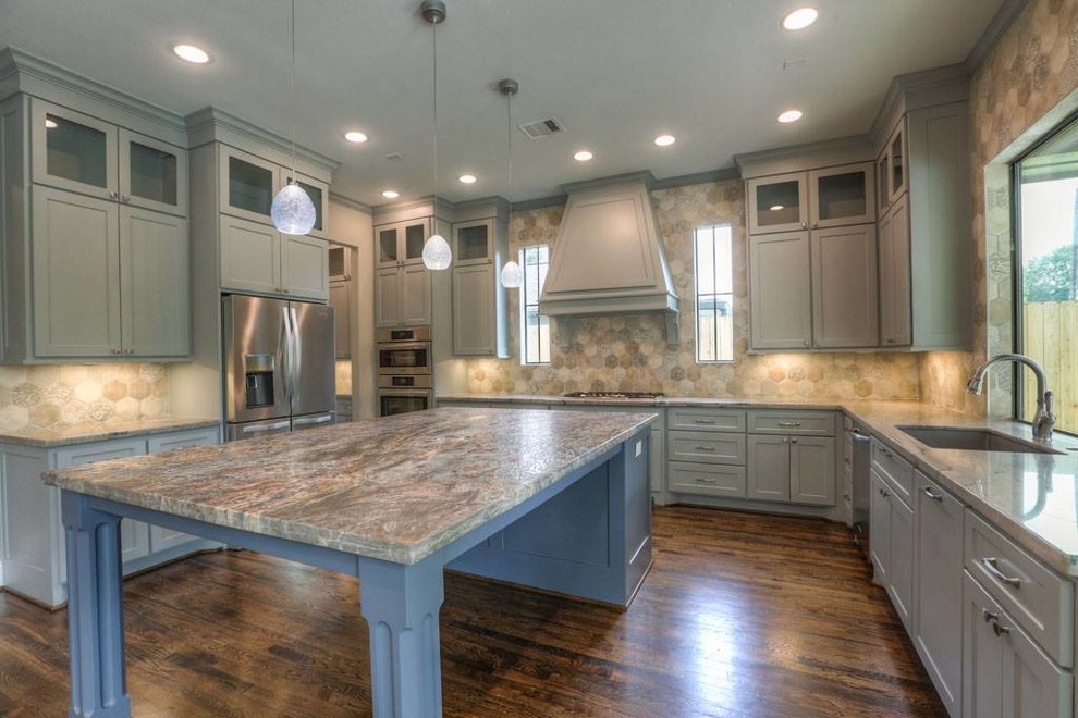 This is an example of a large transitional u-shaped open plan kitchen in Houston with an undermount sink, recessed-panel cabinets, grey cabinets, granite benchtops, beige splashback, stainless steel appliances, dark hardwood floors, with island, brown floor, porcelain splashback and multi-coloured benchtop.