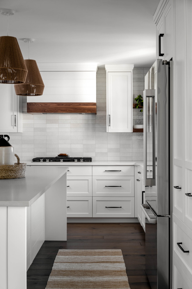 Photo of a mid-sized country l-shaped eat-in kitchen in Toronto with an undermount sink, shaker cabinets, white cabinets, quartz benchtops, white splashback, subway tile splashback, stainless steel appliances, dark hardwood floors, multiple islands, brown floor and grey benchtop.