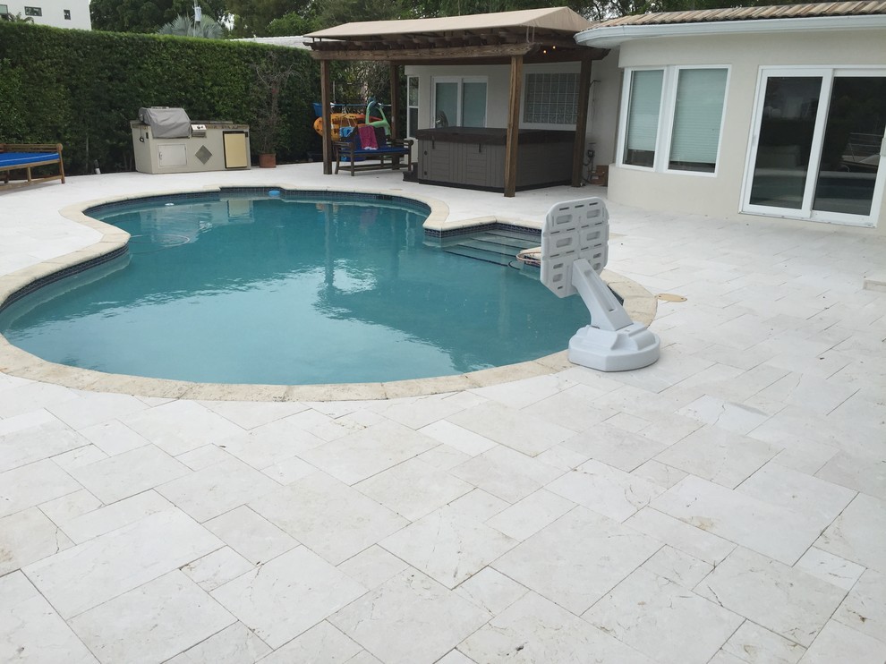 Moderner Pool hinter dem Haus in Nierenform mit Natursteinplatten in Miami