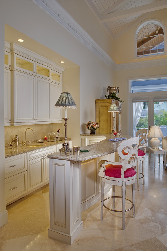 This is an example of a mid-sized tropical galley seated home bar in Miami with an undermount sink, raised-panel cabinets, white cabinets, beige splashback and beige floor.