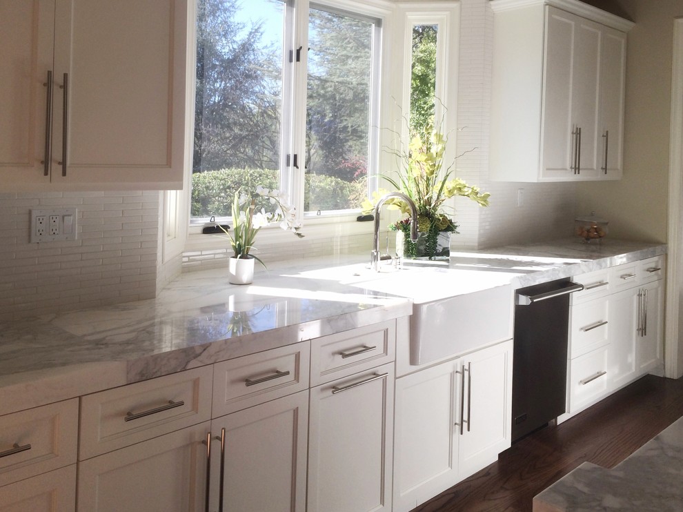 Photo of a large country u-shaped kitchen in Los Angeles with a farmhouse sink, beaded inset cabinets, white cabinets, marble benchtops, white splashback, ceramic splashback, stainless steel appliances, dark hardwood floors, with island and brown floor.