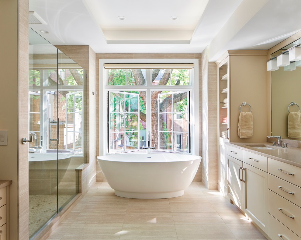 Photo of a contemporary master bathroom in Philadelphia with recessed-panel cabinets, beige cabinets, a freestanding tub, an alcove shower, beige tile, porcelain tile, beige walls, porcelain floors, an undermount sink, engineered quartz benchtops, beige floor, a hinged shower door and beige benchtops.