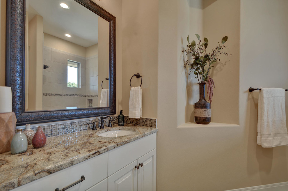Photo of a large traditional kids bathroom in Austin with raised-panel cabinets, white cabinets, a shower/bathtub combo, a one-piece toilet, beige tile, glass tile, beige walls, travertine floors, an undermount sink and granite benchtops.