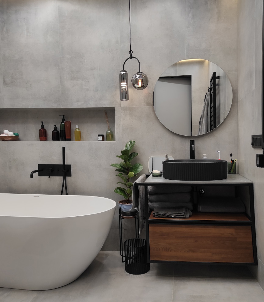 Идея дизайна: серо-белая ванная комната среднего размера в современном стиле с фасадами цвета дерева среднего тона, отдельно стоящей ванной, душем без бортиков, инсталляцией, серой плиткой, керамогранитной плиткой, серыми стенами, бетонным полом, душевой кабиной, подвесной раковиной, столешницей из гранита, серым полом, шторкой для ванной, серой столешницей, зеркалом с подсветкой, тумбой под одну раковину и подвесной тумбой