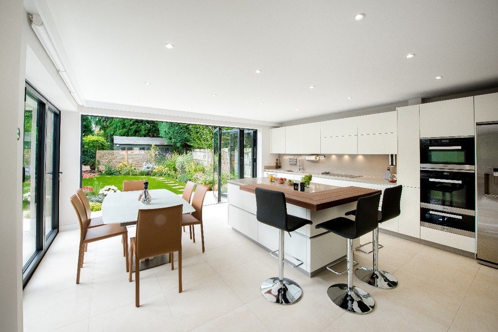 This is an example of a mid-sized modern open plan kitchen in Surrey with flat-panel cabinets, white cabinets, limestone benchtops, stainless steel appliances, limestone floors, a peninsula, beige floor and beige benchtop.