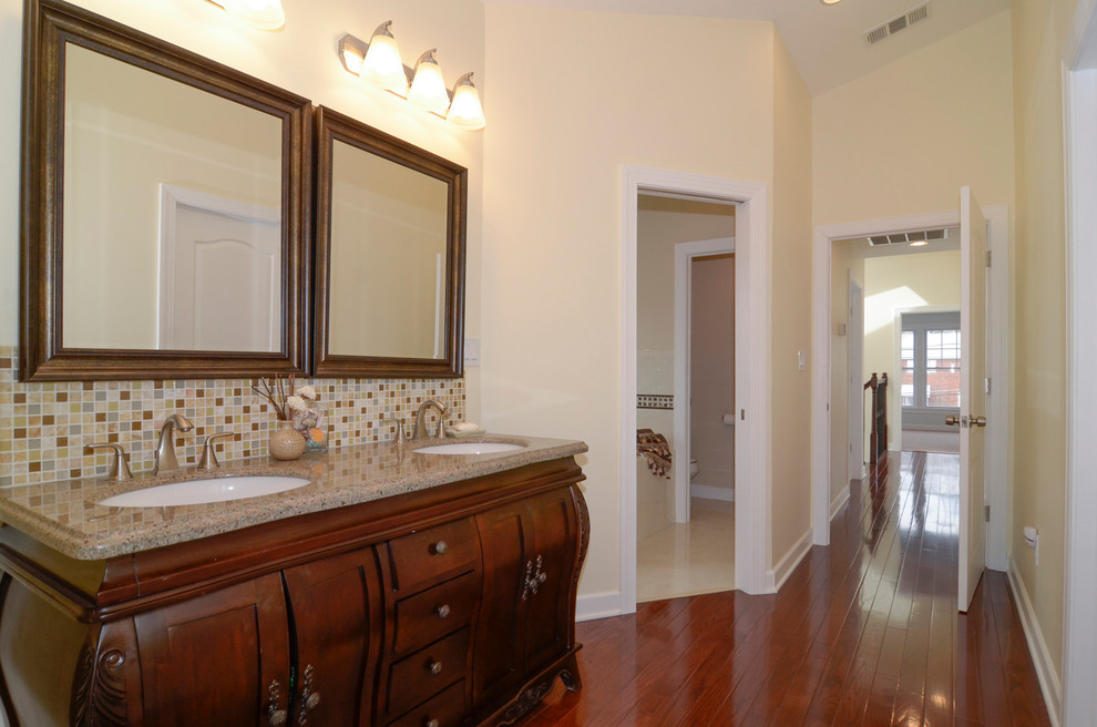 This is an example of a mid-sized arts and crafts master bathroom in DC Metro with furniture-like cabinets, brown cabinets, a two-piece toilet, multi-coloured tile, mosaic tile, yellow walls, dark hardwood floors, an integrated sink, granite benchtops and brown floor.