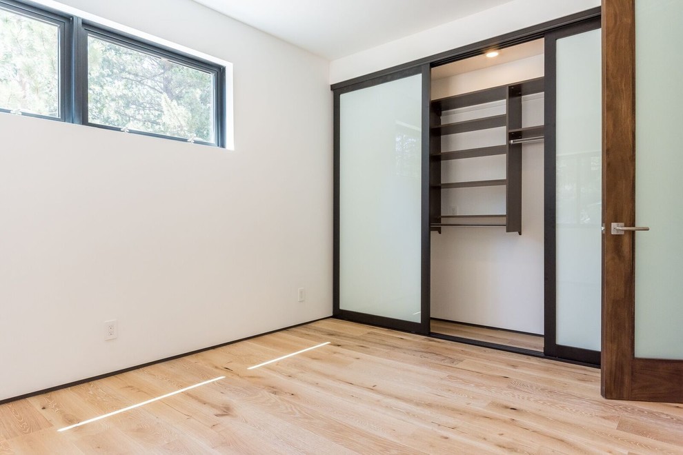 This is an example of a mid-sized modern guest bedroom in Los Angeles with white walls, light hardwood floors and no fireplace.