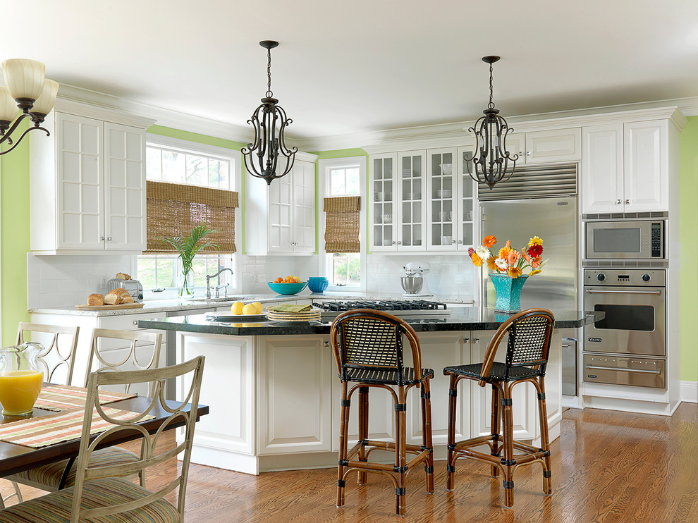 Eat-in kitchen - large coastal l-shaped medium tone wood floor eat-in kitchen idea with raised-panel cabinets, white cabinets, granite countertops, white backsplash, subway tile backsplash, stainless steel appliances, green walls, an undermount sink and an island
