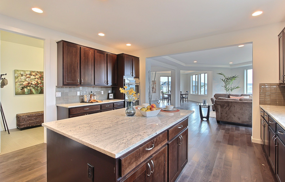 Large transitional u-shaped open concept kitchen photo in Seattle with recessed-panel cabinets, dark wood cabinets, granite countertops, gray backsplash, glass tile backsplash, stainless steel appliances, white walls, engineered wood floors and an island