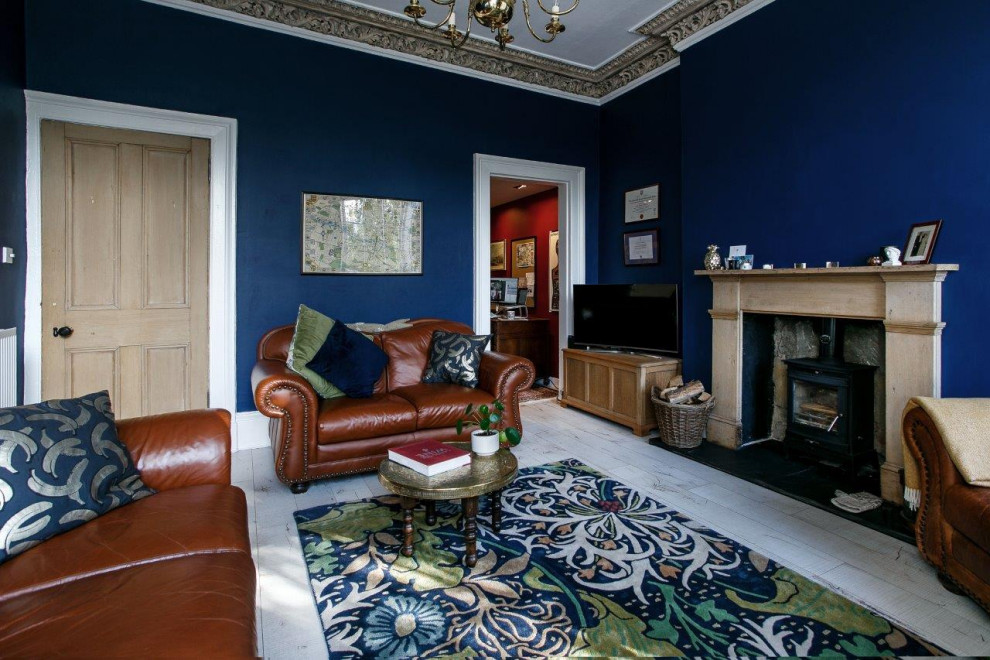 Modelo de salón cerrado ecléctico de tamaño medio con paredes azules, suelo laminado, estufa de leña, marco de chimenea de madera, televisor independiente y suelo blanco