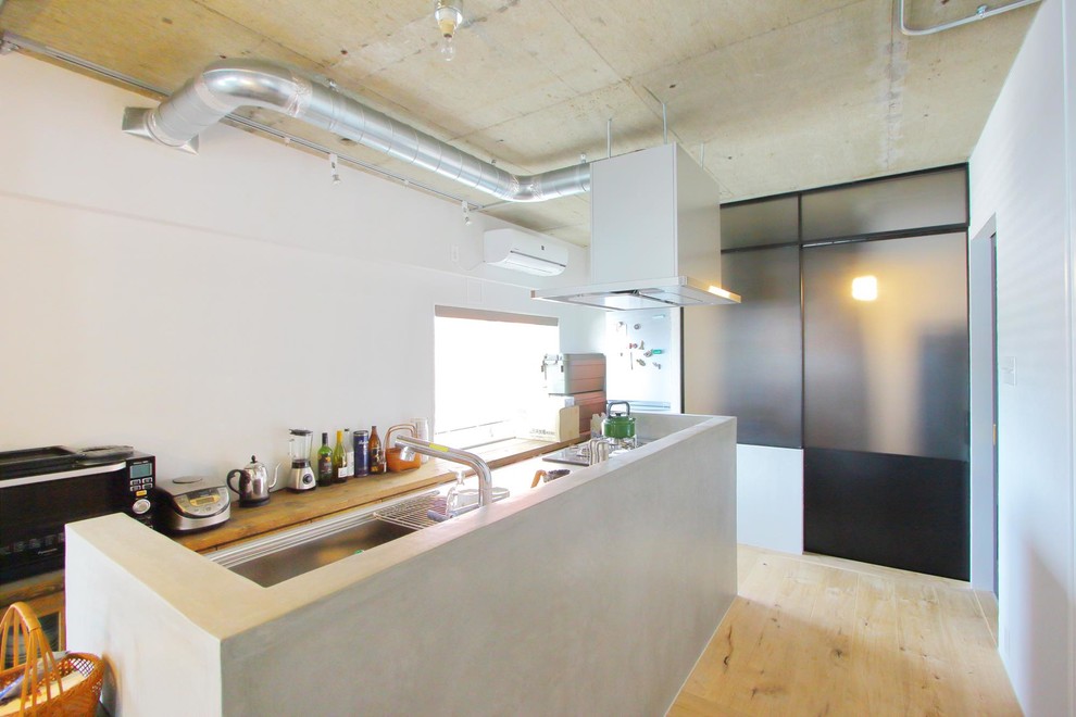 This is an example of an industrial galley open plan kitchen in Tokyo with a single-bowl sink, stainless steel benchtops, light hardwood floors, with island and beige floor.
