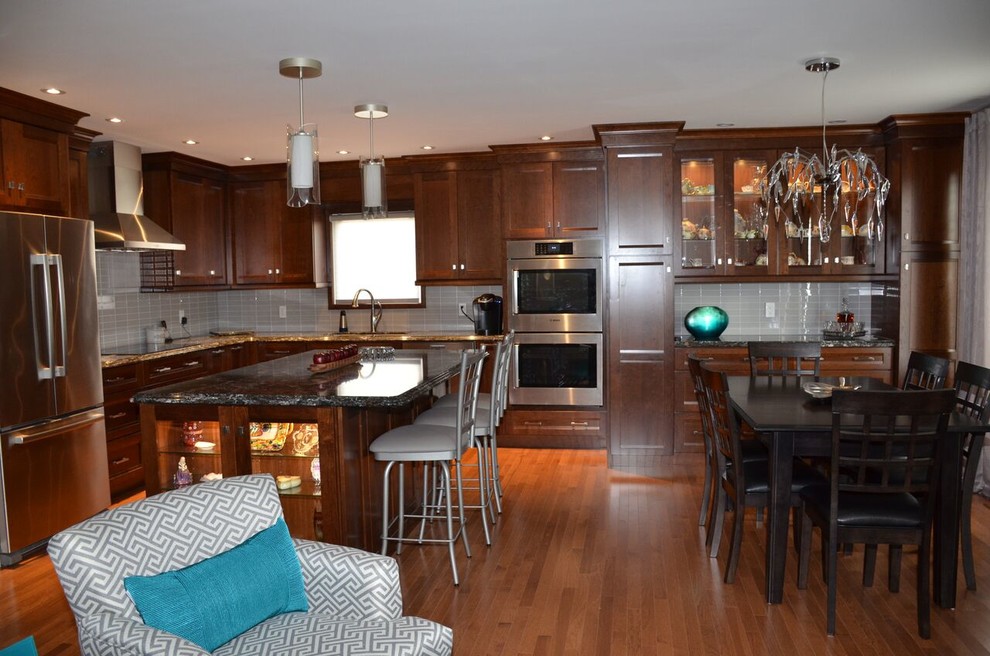 Large transitional l-shaped medium tone wood floor open concept kitchen photo in Toronto with an undermount sink, recessed-panel cabinets, dark wood cabinets, quartzite countertops, gray backsplash, glass tile backsplash, stainless steel appliances and an island