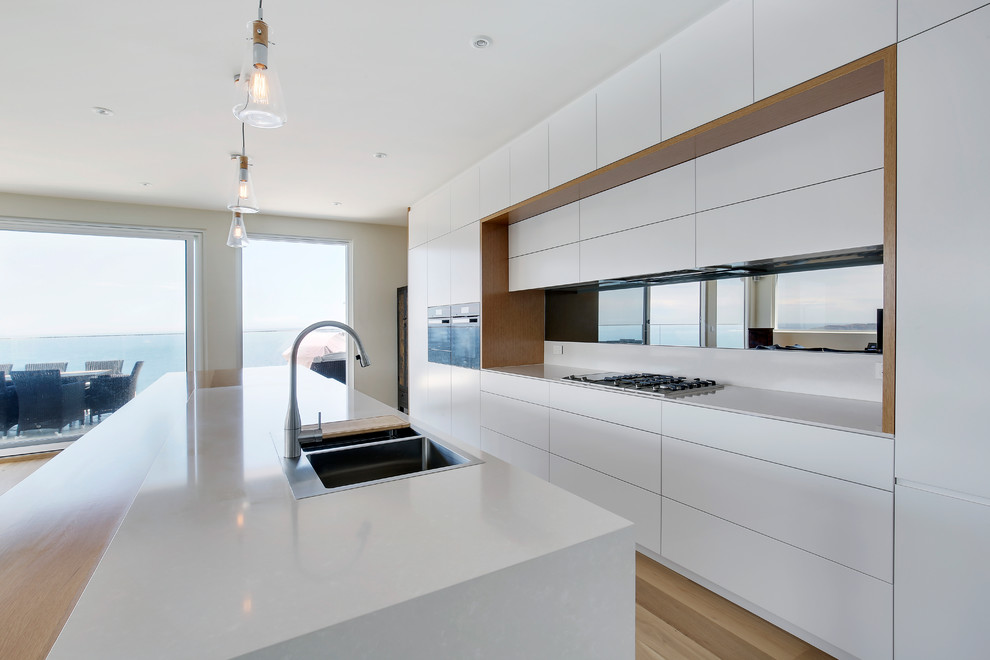 Design ideas for an expansive scandinavian kitchen in Sydney with a double-bowl sink, quartz benchtops, mirror splashback, black appliances and light hardwood floors.