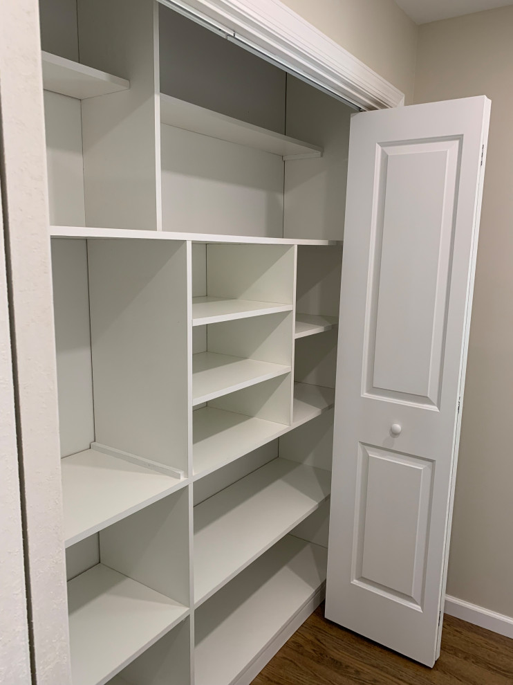 Inspiration for a small transitional storage and wardrobe in New York with open cabinets, white cabinets, medium hardwood floors and brown floor.