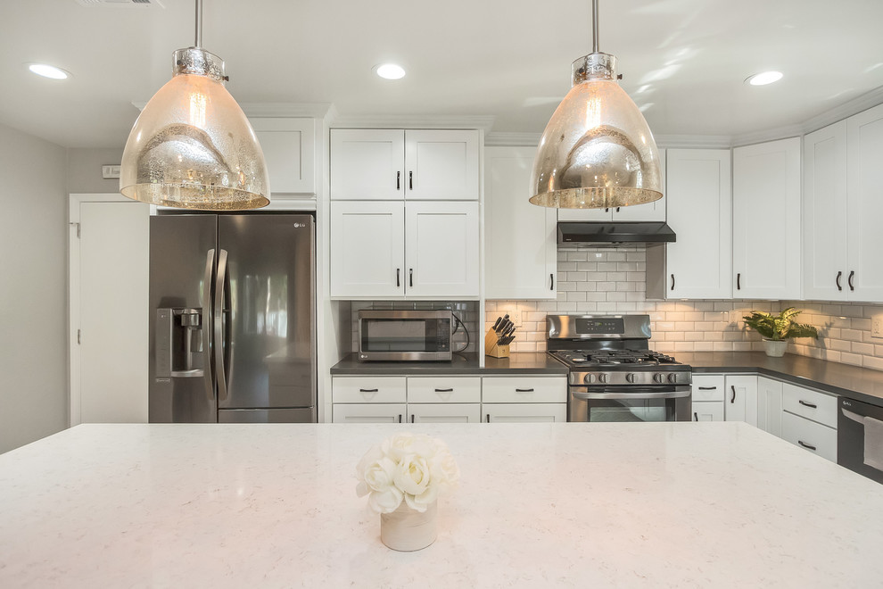 Inspiration for a mid-sized country l-shaped open plan kitchen in Orange County with a farmhouse sink, shaker cabinets, white cabinets, quartz benchtops, white splashback, subway tile splashback, stainless steel appliances, laminate floors and with island.