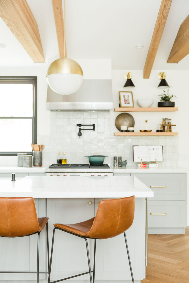 Inspiration for a mid-sized country l-shaped open plan kitchen in San Diego with a farmhouse sink, shaker cabinets, grey cabinets, quartz benchtops, white splashback, terra-cotta splashback, stainless steel appliances, medium hardwood floors, with island, multi-coloured floor and white benchtop.