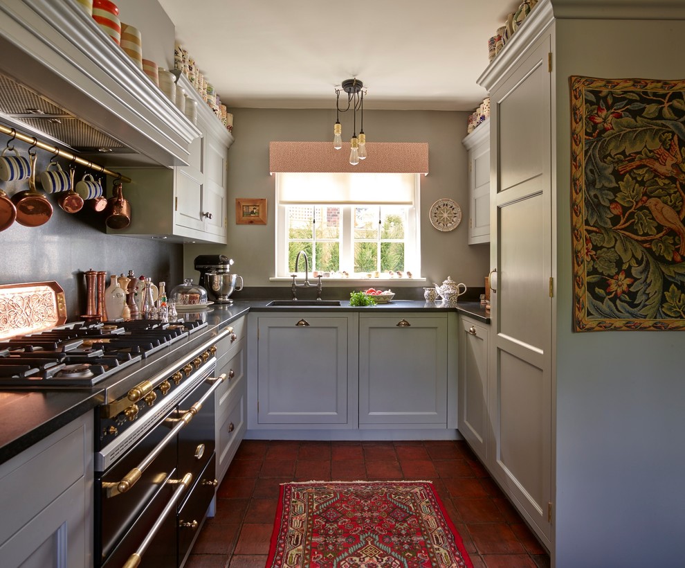 Small traditional u-shaped kitchen in Kent with an undermount sink, shaker cabinets, grey cabinets, black appliances, terra-cotta floors, no island, red floor and black benchtop.