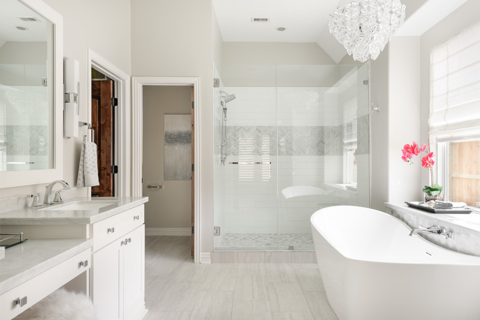 Inspiration for a transitional bathroom in Houston with shaker cabinets, white cabinets, a freestanding tub, an alcove shower, white tile, grey walls, grey floor, a hinged shower door and grey benchtops.
