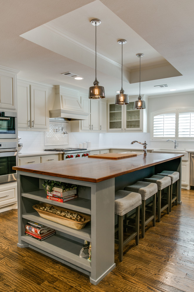 Large traditional u-shaped eat-in kitchen in Dallas with a farmhouse sink, raised-panel cabinets, white cabinets, wood benchtops, white splashback, ceramic splashback, stainless steel appliances, medium hardwood floors and with island.