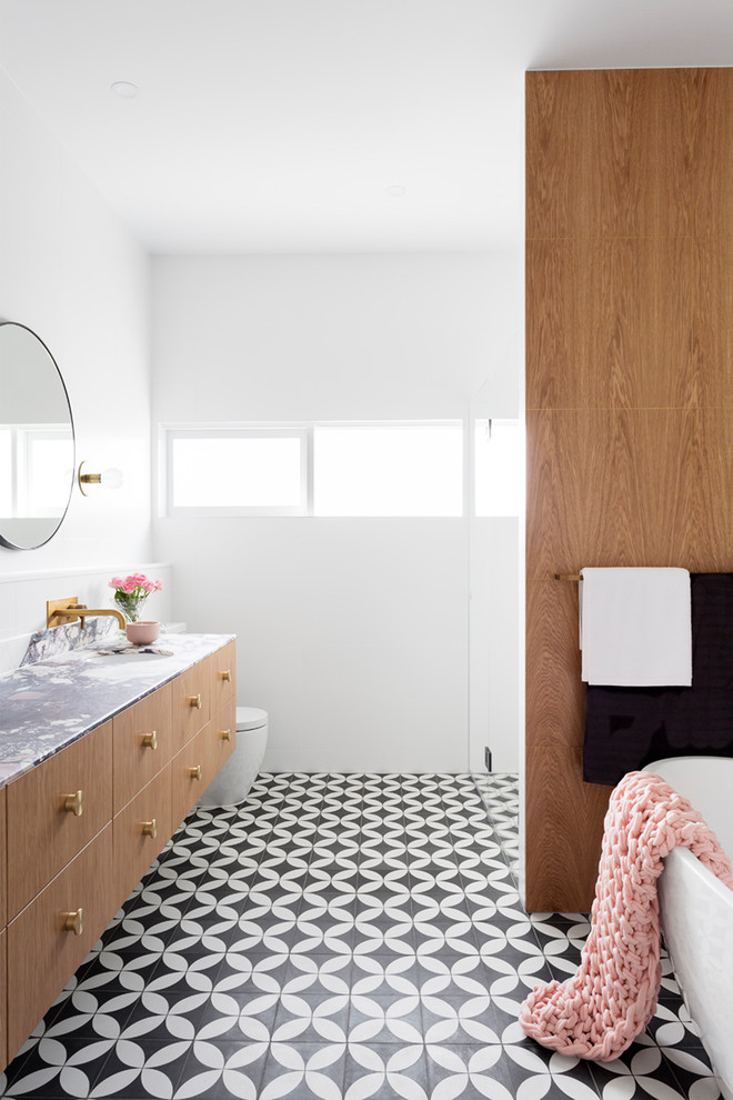 Large contemporary master bathroom in Melbourne with flat-panel cabinets, light wood cabinets, a freestanding tub, an alcove shower, a one-piece toilet, cement tile, cement tiles, an integrated sink, marble benchtops, black floor and white walls.