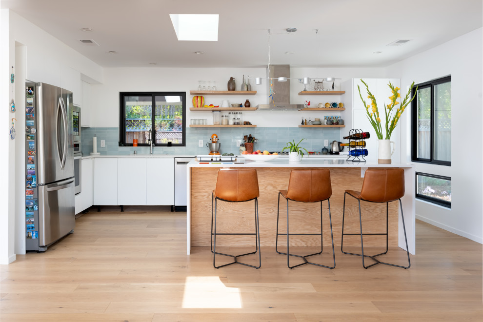 Design ideas for a large contemporary l-shaped open plan kitchen in San Francisco with an undermount sink, flat-panel cabinets, quartz benchtops, blue splashback, ceramic splashback, stainless steel appliances, light hardwood floors, with island, white benchtop, white cabinets and beige floor.