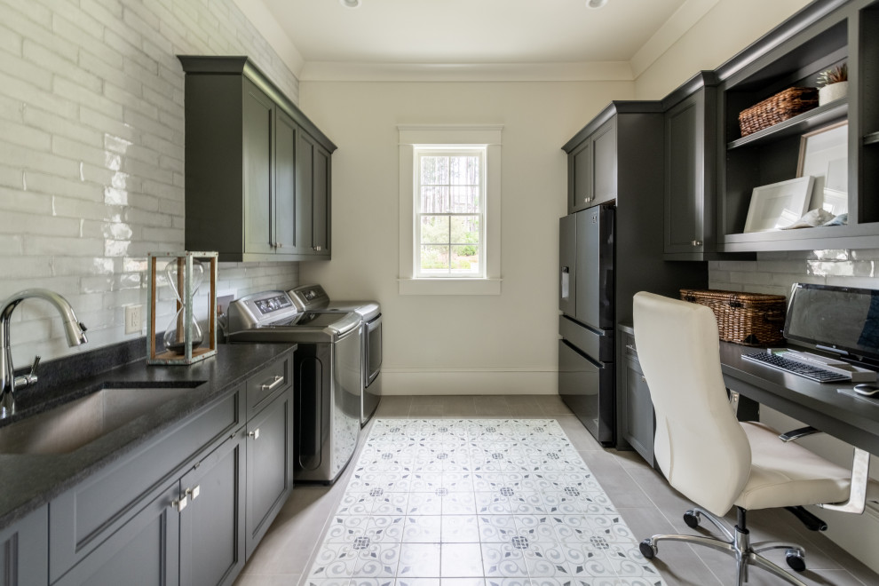 This is an example of a contemporary utility room in Atlanta with an undermount sink, recessed-panel cabinets, grey cabinets, granite benchtops, white splashback, ceramic splashback, white walls, ceramic floors, a side-by-side washer and dryer, grey floor and black benchtop.