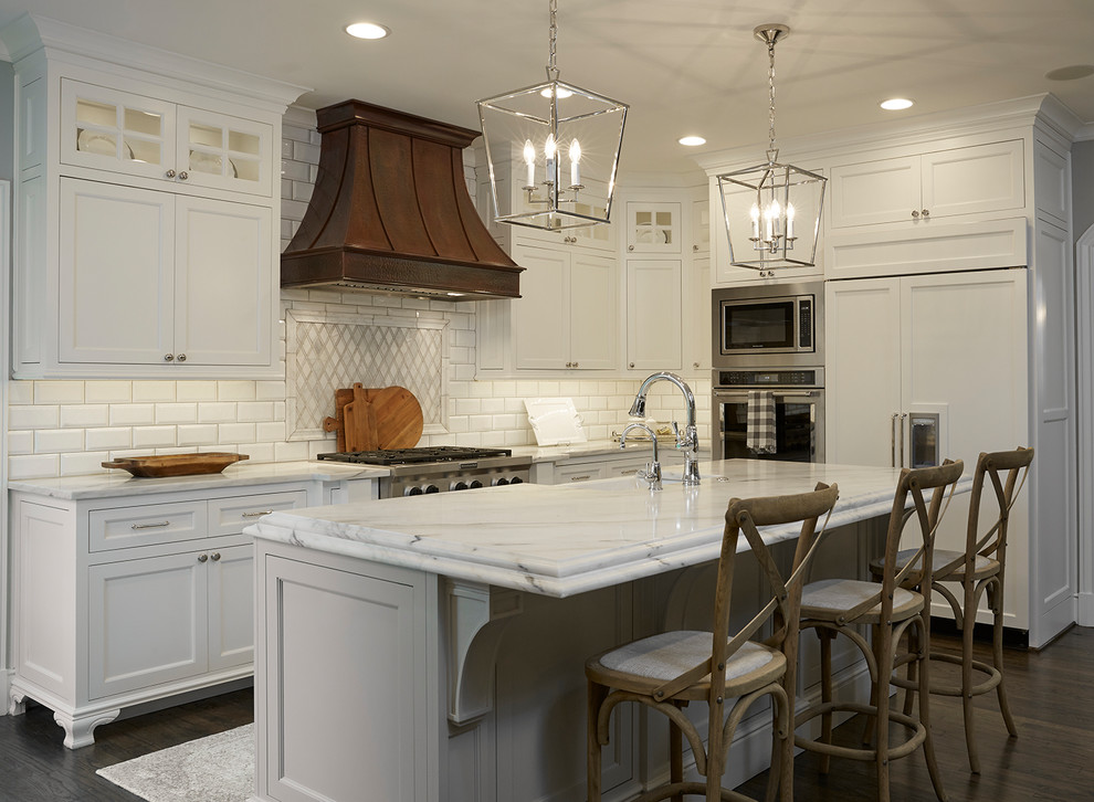 Design ideas for a traditional l-shaped kitchen in Dallas with a farmhouse sink, shaker cabinets, white cabinets, white splashback, subway tile splashback, dark hardwood floors, with island and brown floor.
