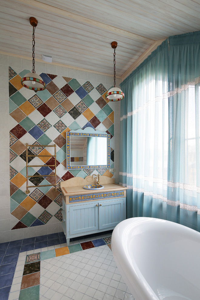 This is an example of a mid-sized mediterranean master bathroom in Moscow with recessed-panel cabinets, blue cabinets, a freestanding tub, multi-coloured tile, a drop-in sink, multi-coloured floor and beige benchtops.