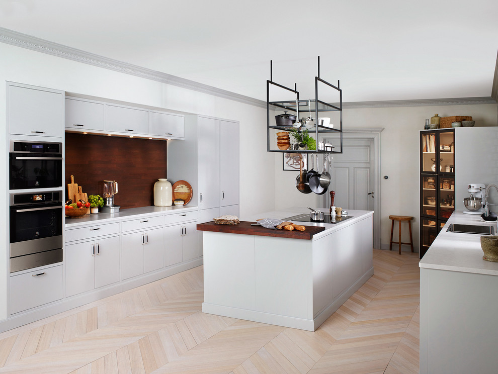 This is an example of a large modern u-shaped open plan kitchen in Stockholm with a drop-in sink, flat-panel cabinets, white cabinets, stainless steel appliances, light hardwood floors and with island.