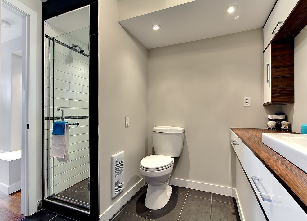 Small modern bathroom in Montreal with a vessel sink, flat-panel cabinets, brown cabinets, laminate benchtops, an alcove tub, an alcove shower, a two-piece toilet, gray tile, ceramic tile, beige walls and ceramic floors.