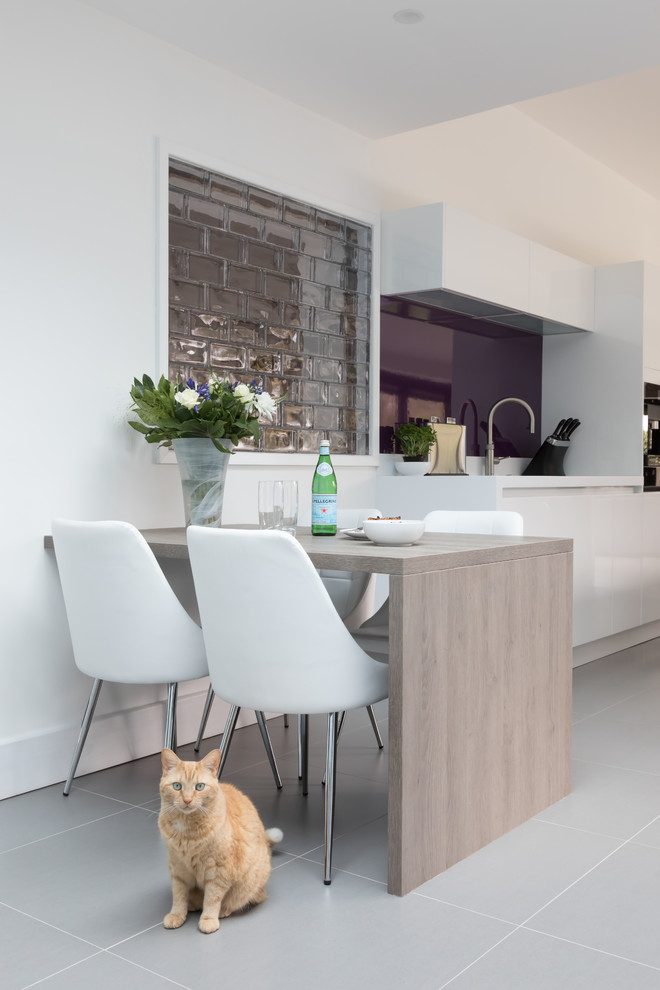 Mid-sized contemporary eat-in kitchen in West Midlands with flat-panel cabinets, white cabinets, black appliances, ceramic floors, with island and grey floor.