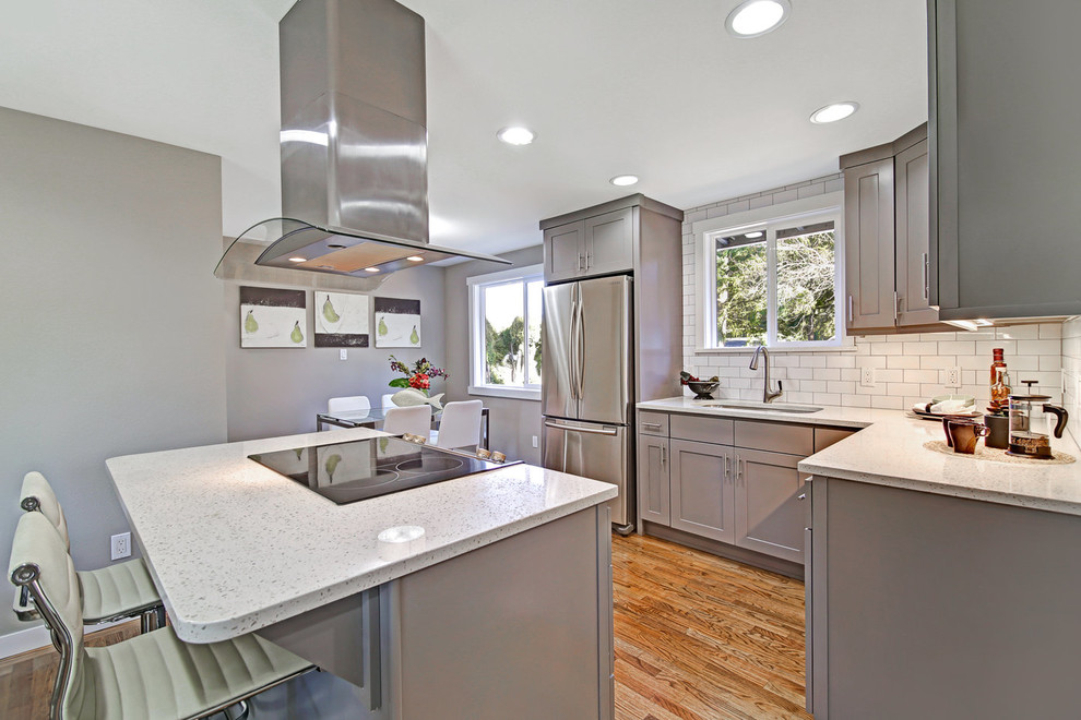 Eat-in kitchen - mid-sized transitional l-shaped medium tone wood floor and brown floor eat-in kitchen idea in Seattle with an undermount sink, shaker cabinets, gray cabinets, quartz countertops, white backsplash, ceramic backsplash, stainless steel appliances, an island and white countertops