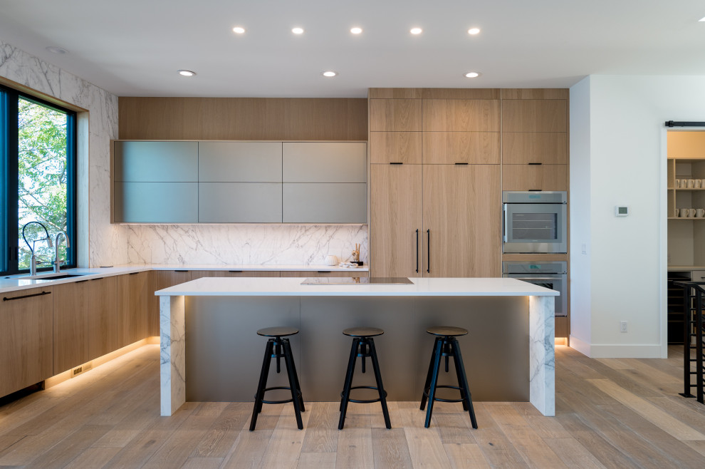 Example of a large trendy l-shaped light wood floor and brown floor open concept kitchen design in Phoenix with an undermount sink, flat-panel cabinets, light wood cabinets, quartz countertops, white backsplash, stone slab backsplash, paneled appliances, an island and white countertops