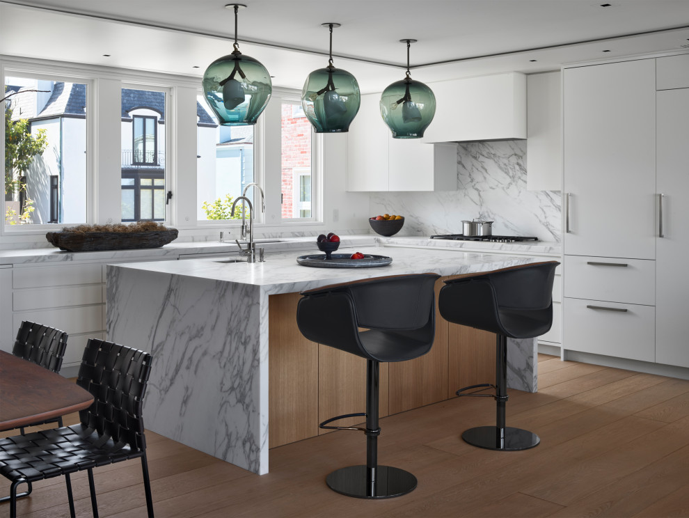 Large contemporary l-shaped eat-in kitchen in San Francisco with flat-panel cabinets, white cabinets, marble benchtops, white splashback, marble splashback, with island, white benchtop, an undermount sink, panelled appliances, medium hardwood floors and brown floor.