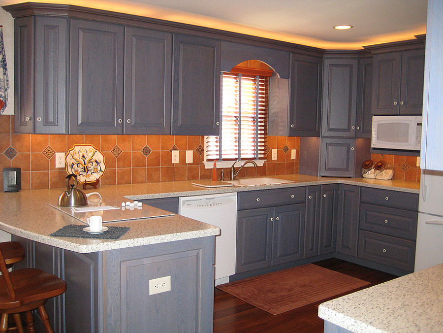 Inspiration for a mid-sized transitional u-shaped medium tone wood floor eat-in kitchen remodel with an integrated sink, raised-panel cabinets, blue cabinets, solid surface countertops, brown backsplash, terra-cotta backsplash, white appliances and a peninsula