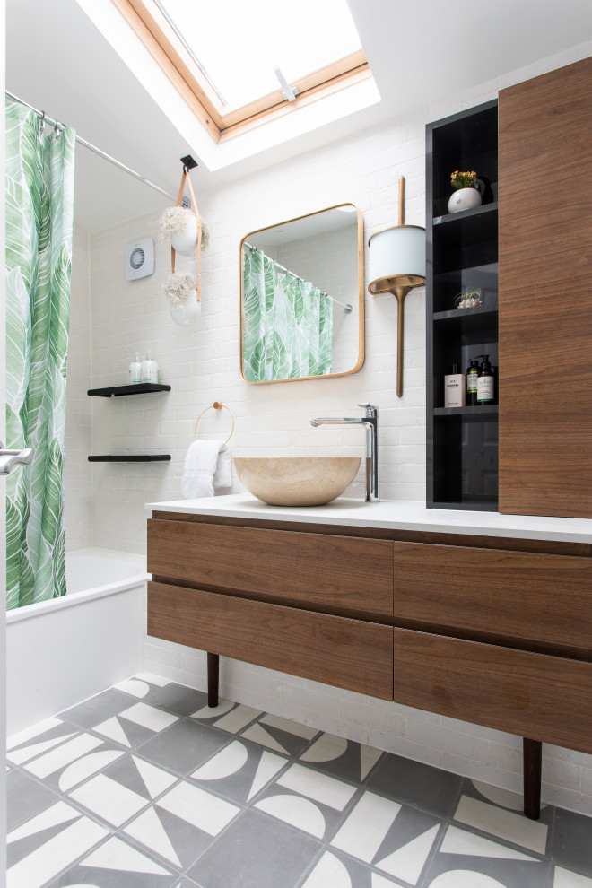 Mid-sized contemporary kids bathroom in London with flat-panel cabinets, a drop-in tub, a shower/bathtub combo, beige tile, porcelain tile, cement tiles, a vessel sink, solid surface benchtops, grey floor, a shower curtain, white benchtops, a single vanity, a built-in vanity and medium wood cabinets.