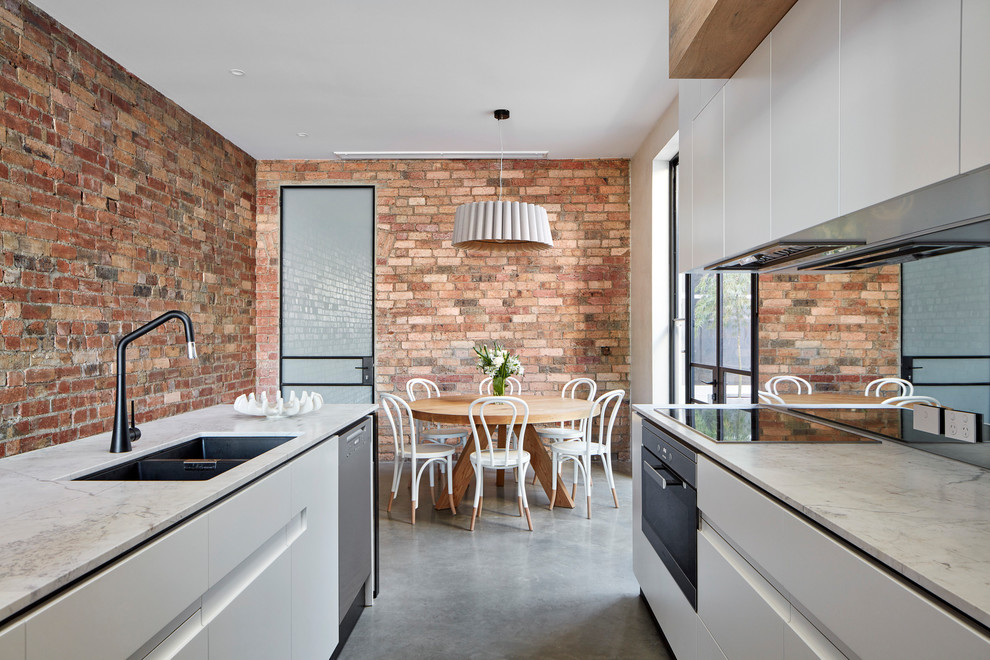 This is an example of a small contemporary galley eat-in kitchen in Melbourne with an undermount sink, flat-panel cabinets, white cabinets, marble benchtops, mirror splashback, black appliances, concrete floors, with island and grey floor.