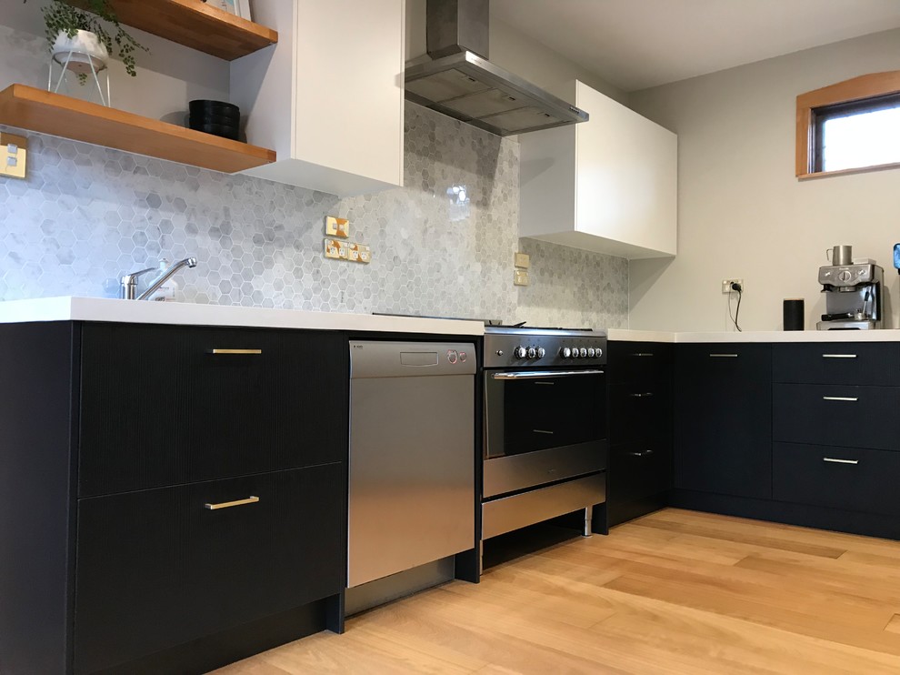 Mid-sized contemporary l-shaped separate kitchen in Christchurch with a single-bowl sink, flat-panel cabinets, black cabinets, concrete benchtops, grey splashback, mosaic tile splashback, stainless steel appliances, light hardwood floors, no island, brown floor and white benchtop.