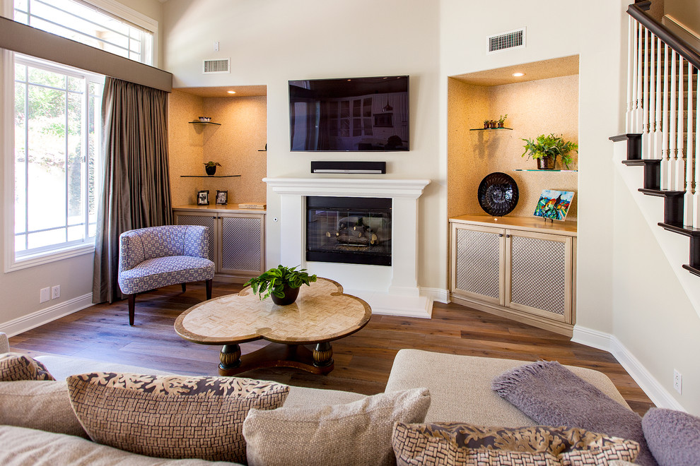 Design ideas for a mid-sized traditional open concept family room in San Diego with beige walls, medium hardwood floors, a hanging fireplace, a plaster fireplace surround and a wall-mounted tv.