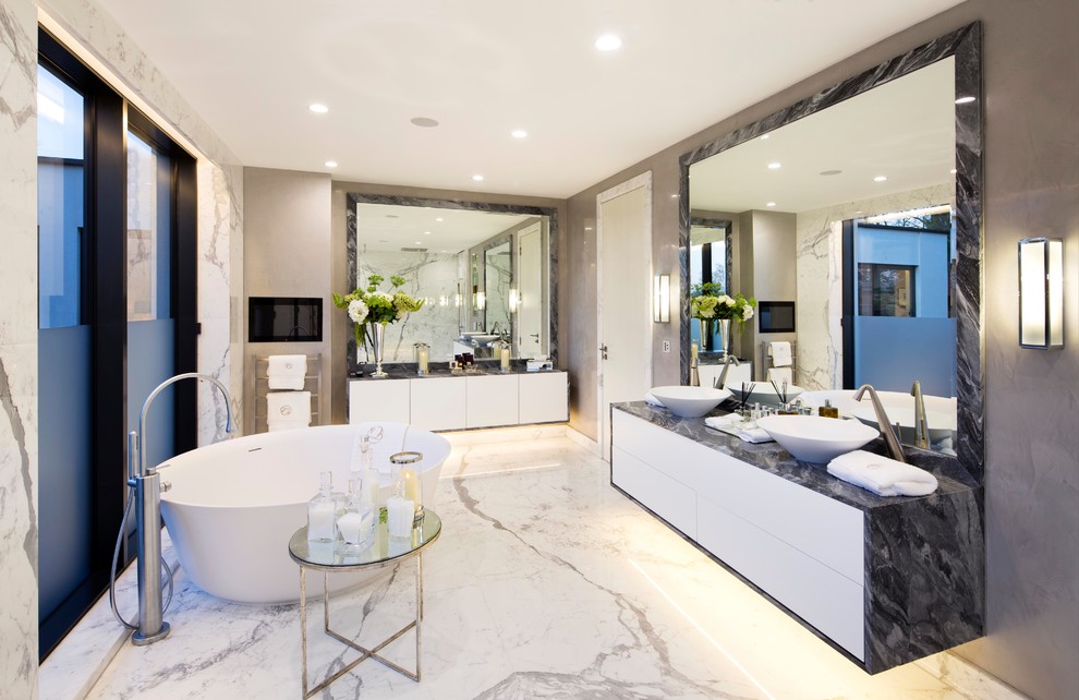 Photo of a large contemporary master bathroom in London with flat-panel cabinets, white cabinets, a freestanding tub, marble floors, marble benchtops, white floor, black benchtops, grey walls, a vessel sink and beige tile.