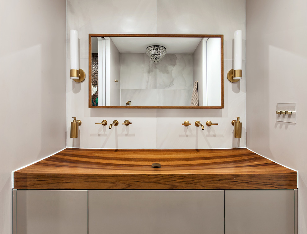 This is an example of a mid-sized contemporary master bathroom in New York with flat-panel cabinets, beige cabinets, a japanese tub, beige tile, porcelain tile, beige walls, porcelain floors, a trough sink, wood benchtops, an open shower, a one-piece toilet and an open shower.